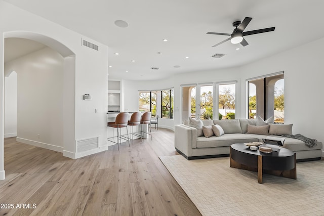 living area featuring light wood finished floors, visible vents, and arched walkways