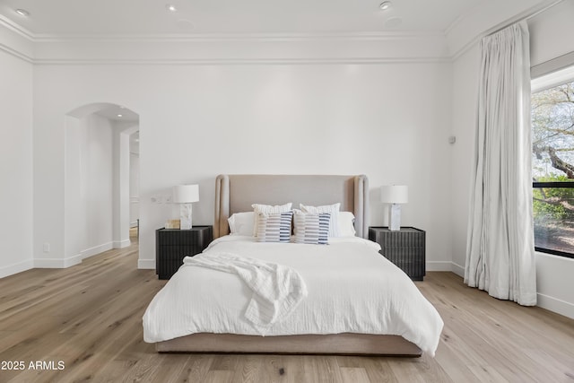 bedroom with baseboards, arched walkways, light wood-style flooring, and ornamental molding