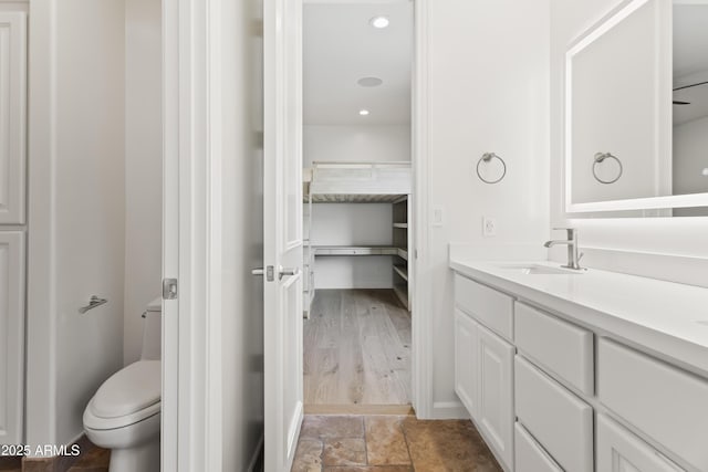 full bathroom with a spacious closet, toilet, recessed lighting, stone finish floor, and vanity