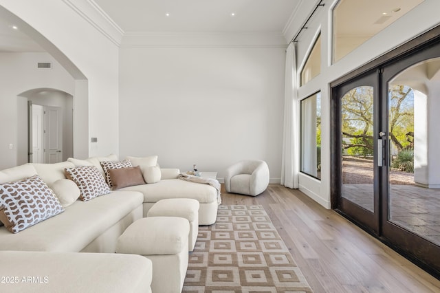 living room featuring visible vents, ornamental molding, light wood-style flooring, french doors, and arched walkways