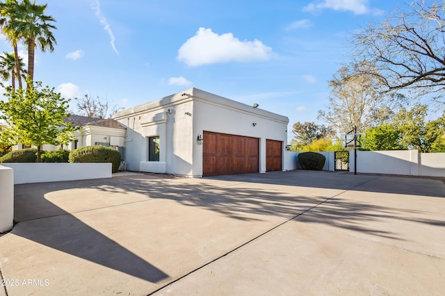 view of side of property featuring a gate, stucco siding, concrete driveway, and fence