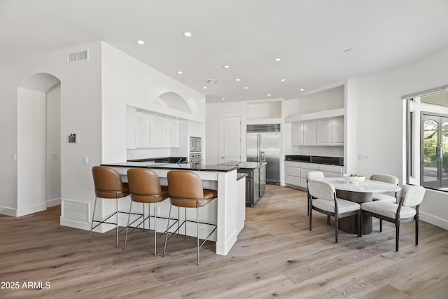 kitchen with visible vents, a peninsula, built in appliances, white cabinetry, and dark countertops