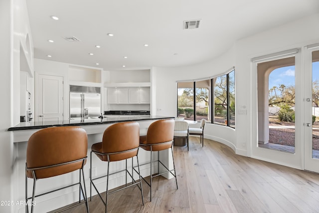 kitchen featuring a breakfast bar area, visible vents, stainless steel built in fridge, dark countertops, and light wood-type flooring