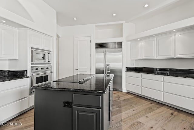 kitchen featuring light wood finished floors, built in appliances, white cabinets, and dark stone counters