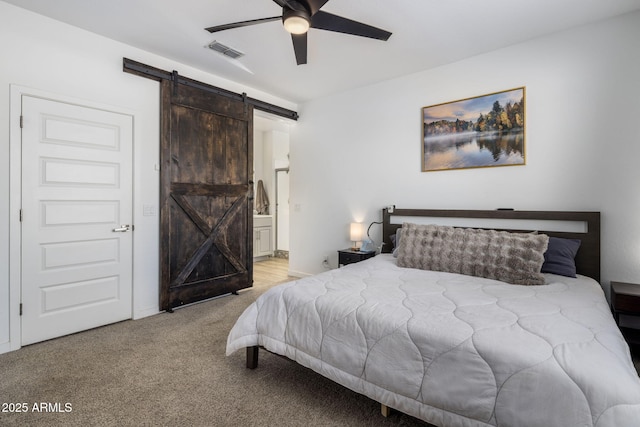 carpeted bedroom featuring a barn door, ceiling fan, and ensuite bathroom