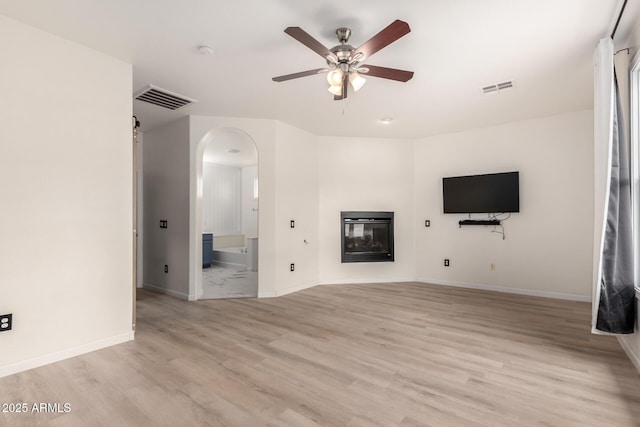 1162 S Agnes Ln, Gilbert, AZ 85296 - unfurnished living room featuring arched walkways, a ceiling fan, light wood-style floors, and a glass covered fireplace