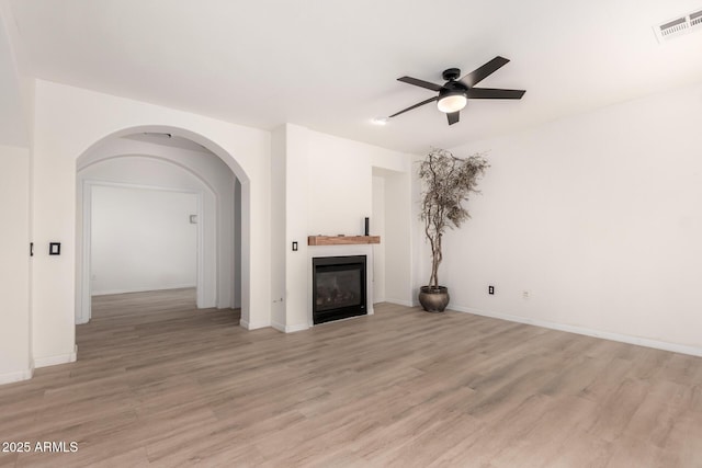 1162 S Agnes Ln, Gilbert, AZ 85296 - unfurnished living room with a ceiling fan, light wood-style floors, a glass covered fireplace, and arched walkways