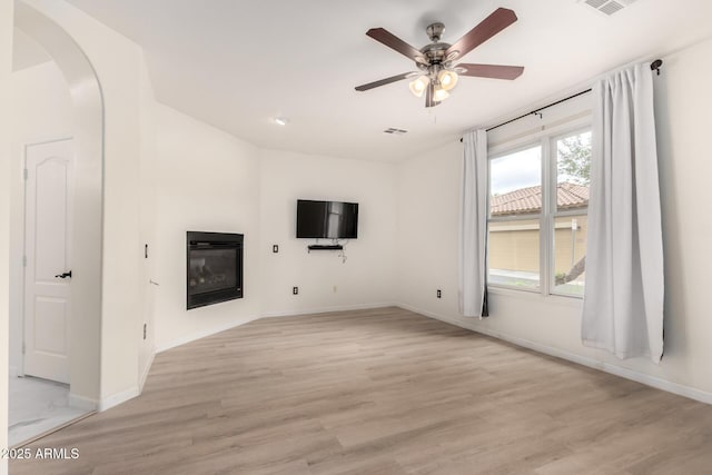 1162 S Agnes Ln, Gilbert, AZ 85296 - unfurnished living room featuring a glass covered fireplace, a ceiling fan, light wood-style floors, baseboards, and arched walkways