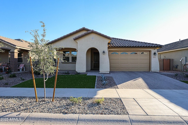 mediterranean / spanish-style home with decorative driveway, an attached garage, a tile roof, and stucco siding