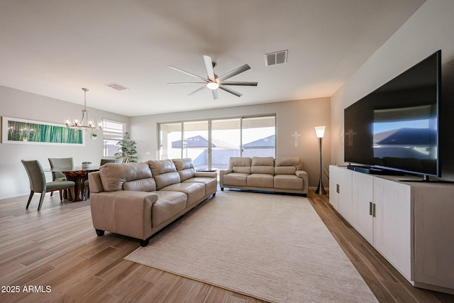 living room featuring ceiling fan with notable chandelier, visible vents, and wood finished floors