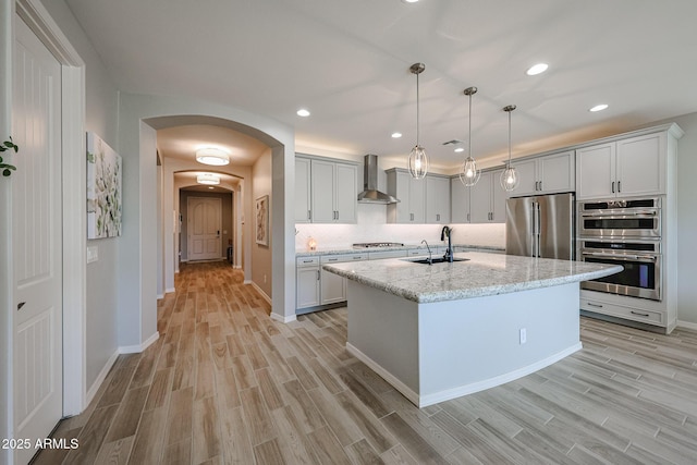 kitchen featuring arched walkways, tasteful backsplash, appliances with stainless steel finishes, a sink, and wall chimney range hood