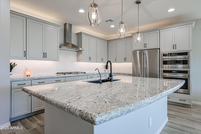 kitchen with light stone counters, stainless steel appliances, wood tiled floor, a sink, and wall chimney range hood