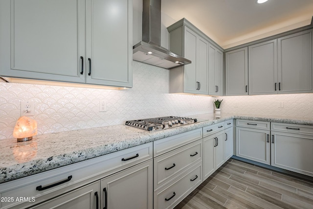 kitchen featuring wall chimney range hood, tasteful backsplash, wood tiled floor, and light stone counters