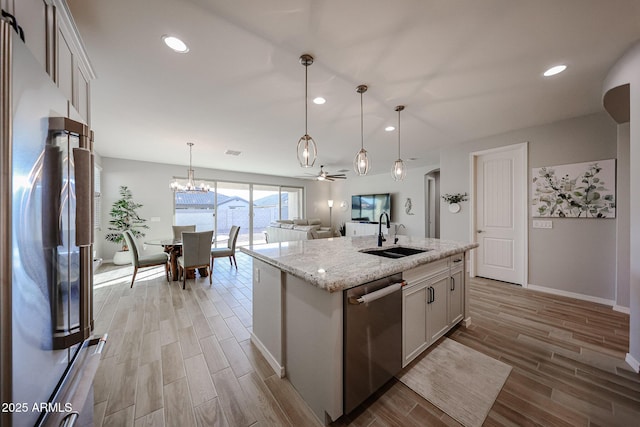 kitchen featuring light stone counters, hanging light fixtures, stainless steel appliances, wood finish floors, and a sink