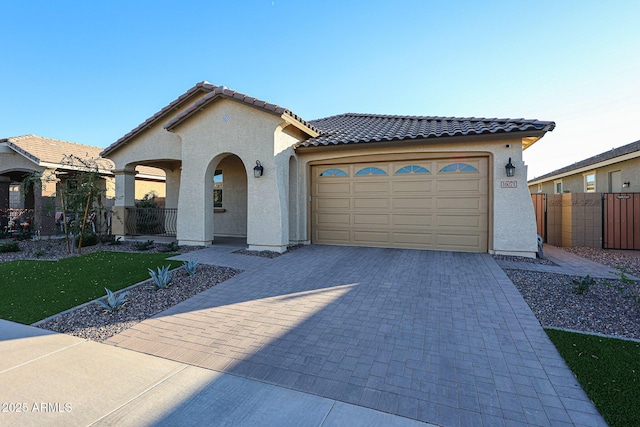 mediterranean / spanish house with decorative driveway, stucco siding, fence, a garage, and a tiled roof