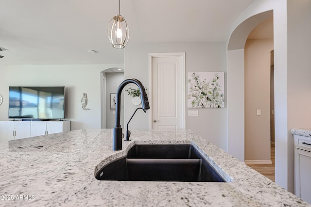 kitchen featuring light stone counters, arched walkways, hanging light fixtures, a sink, and wood finished floors