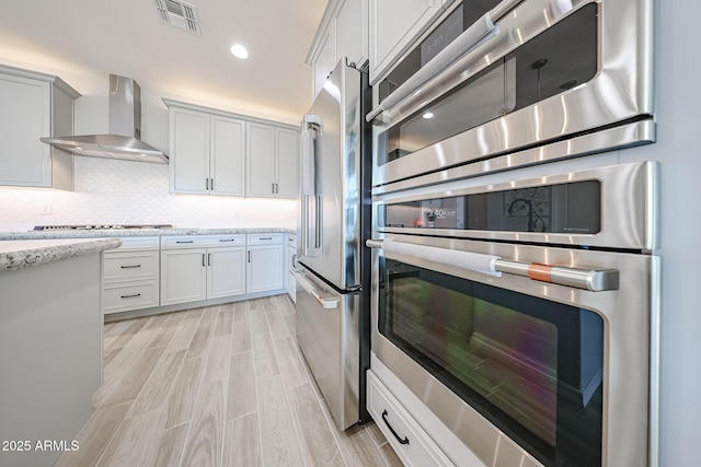 kitchen featuring visible vents, decorative backsplash, wall chimney exhaust hood, stainless steel appliances, and wood finish floors