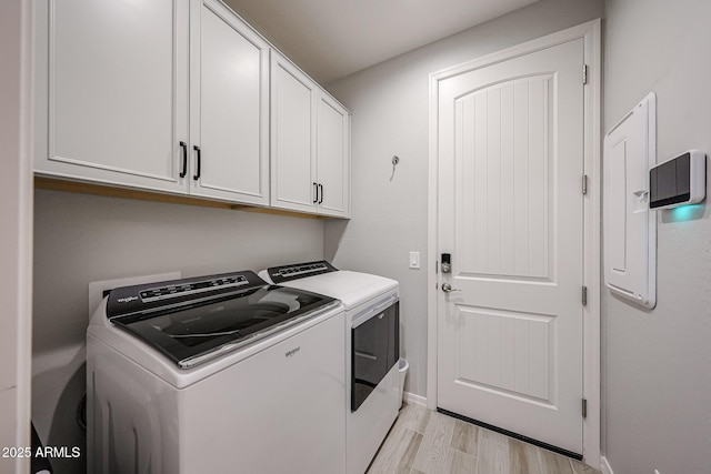 laundry room featuring light wood-type flooring, baseboards, cabinet space, and washing machine and clothes dryer