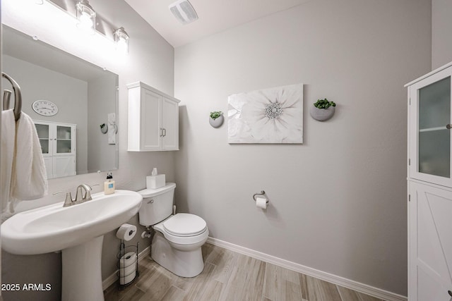 half bath featuring baseboards, visible vents, toilet, and wood finished floors