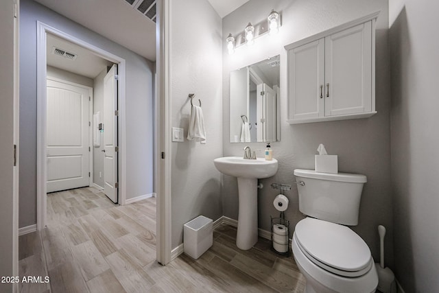 bathroom featuring toilet, baseboards, visible vents, and wood finished floors