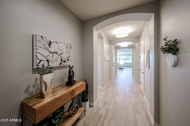 hall featuring light wood-type flooring, baseboards, and arched walkways