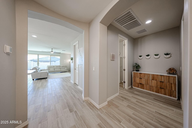 hallway featuring arched walkways, recessed lighting, visible vents, light wood-style floors, and baseboards