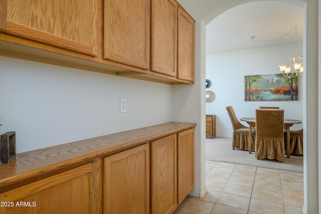 17640 W Babbitt Dr, Surprise, AZ 85374 - kitchen with brown cabinets, light tile patterned floors, a notable chandelier, light carpet, and arched walkways