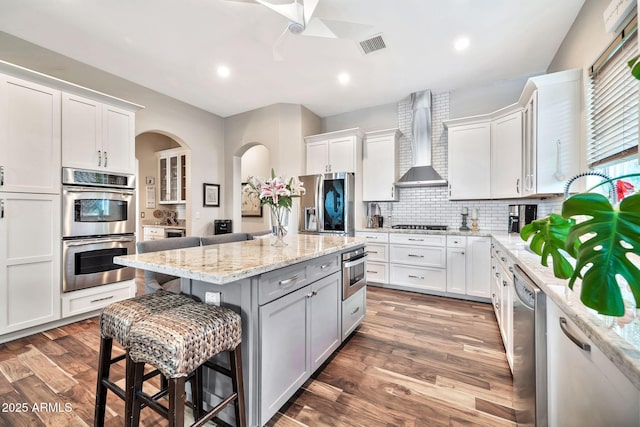 kitchen featuring wall chimney range hood, light stone countertops, white cabinets, and a kitchen island