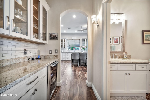 bar with wine cooler, sink, tasteful backsplash, light stone counters, and white cabinets