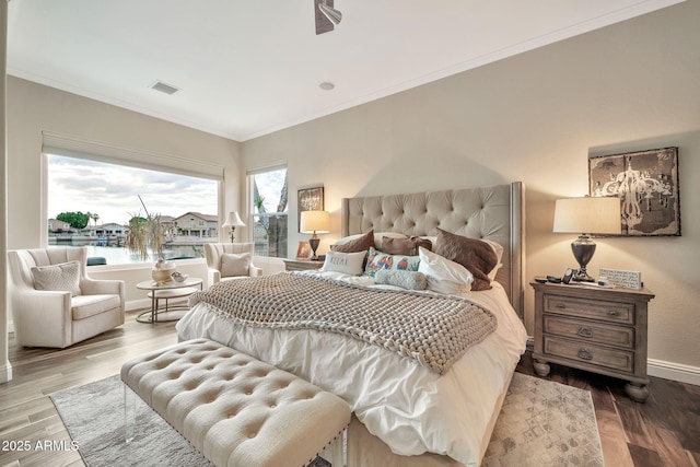 bedroom with hardwood / wood-style flooring, ornamental molding, and a water view