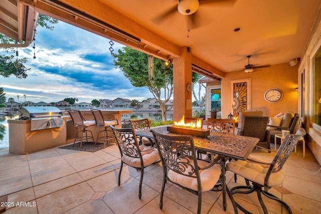 view of patio featuring exterior kitchen, ceiling fan, an outdoor fire pit, a grill, and exterior bar