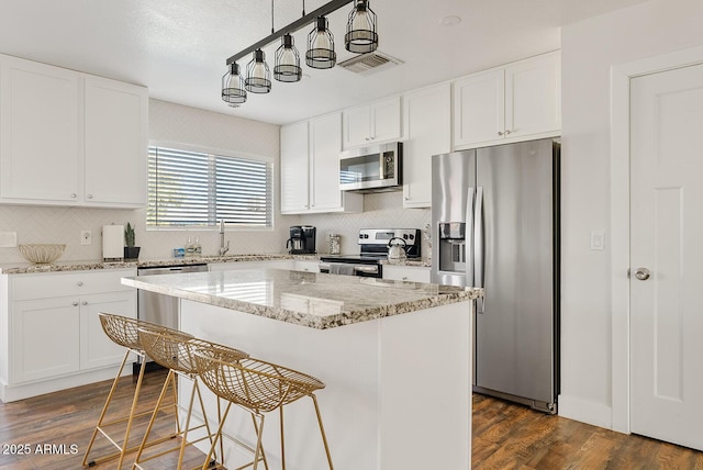 kitchen featuring a kitchen island, dark hardwood / wood-style floors, decorative light fixtures, white cabinets, and stainless steel appliances