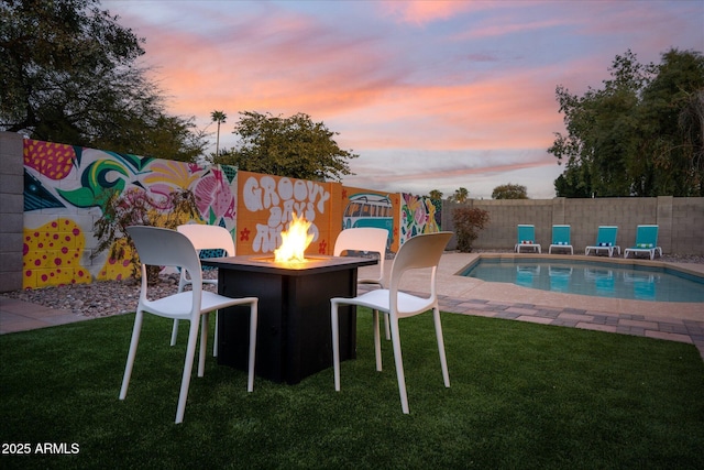 pool at dusk featuring a lawn and an outdoor fire pit