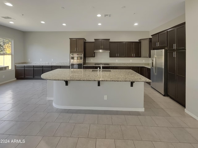 kitchen with appliances with stainless steel finishes, a kitchen breakfast bar, light stone counters, sink, and a center island with sink