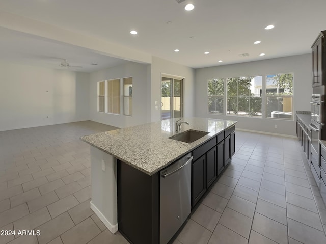 kitchen with ceiling fan, sink, stainless steel appliances, light stone counters, and a center island with sink