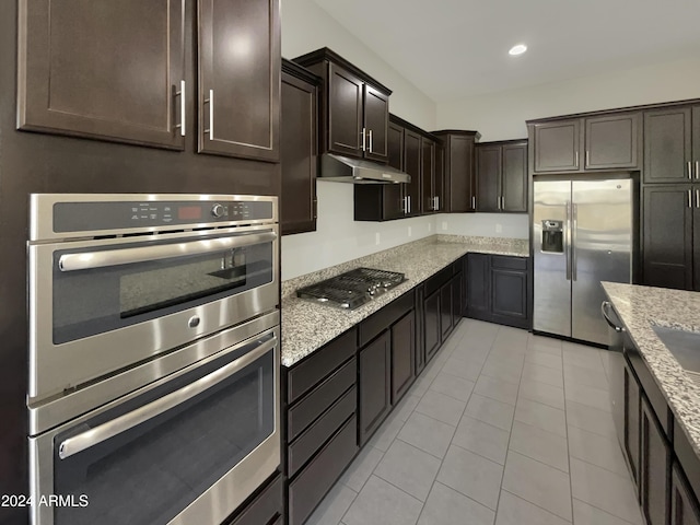 kitchen featuring light stone countertops, appliances with stainless steel finishes, dark brown cabinetry, and light tile patterned floors