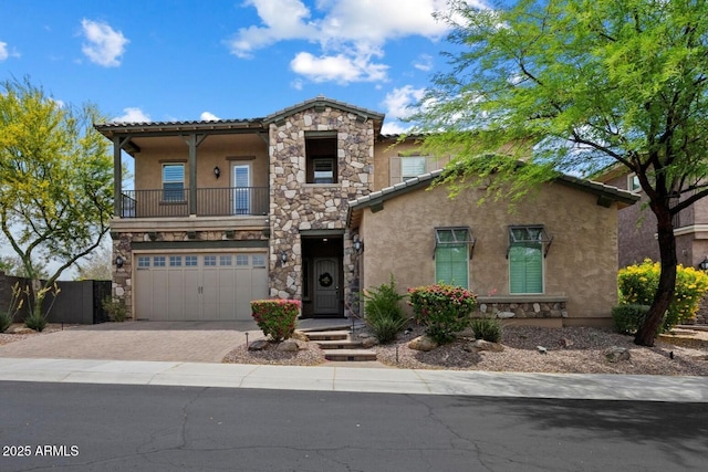 view of front of property featuring stone siding, an attached garage, stucco siding, decorative driveway, and a balcony