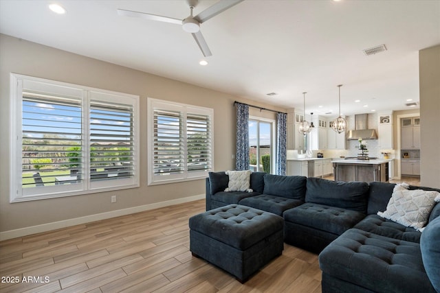 living area featuring recessed lighting, baseboards, visible vents, ceiling fan with notable chandelier, and light wood-style floors
