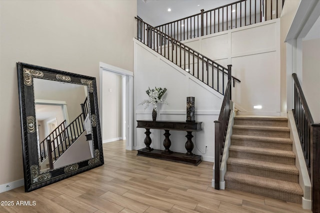 stairway with baseboards, wood finished floors, and a towering ceiling