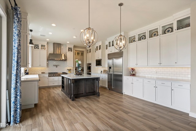 kitchen with built in appliances, wall chimney range hood, a notable chandelier, and backsplash