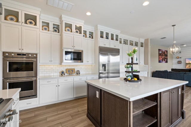 kitchen with open shelves, white cabinetry, built in appliances, backsplash, and light countertops