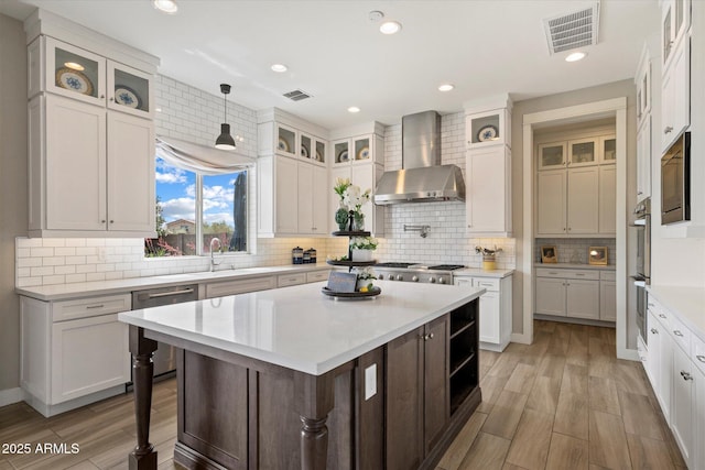 kitchen featuring a center island, visible vents, wall chimney exhaust hood, light countertops, and appliances with stainless steel finishes