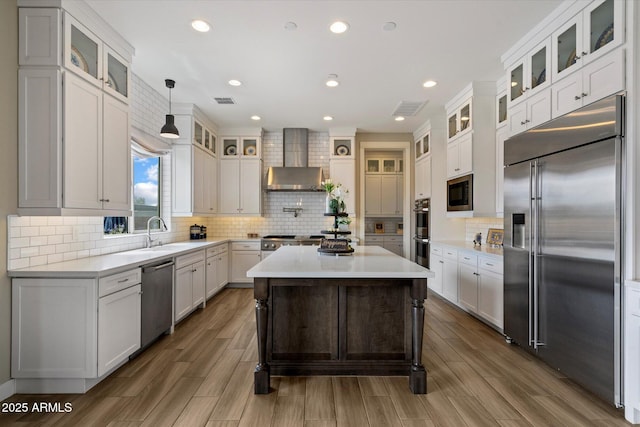 kitchen featuring a sink, built in appliances, tasteful backsplash, wall chimney range hood, and visible vents