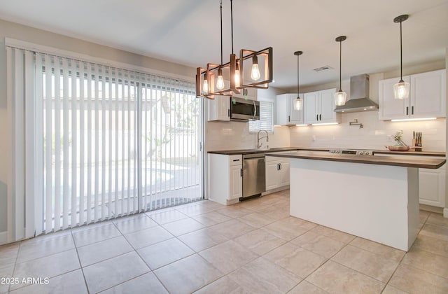 kitchen featuring white cabinetry, wall chimney range hood, stainless steel appliances, tasteful backsplash, and hanging light fixtures