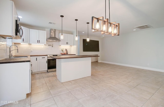 kitchen featuring pendant lighting, a kitchen island, white cabinetry, stainless steel appliances, and wall chimney exhaust hood