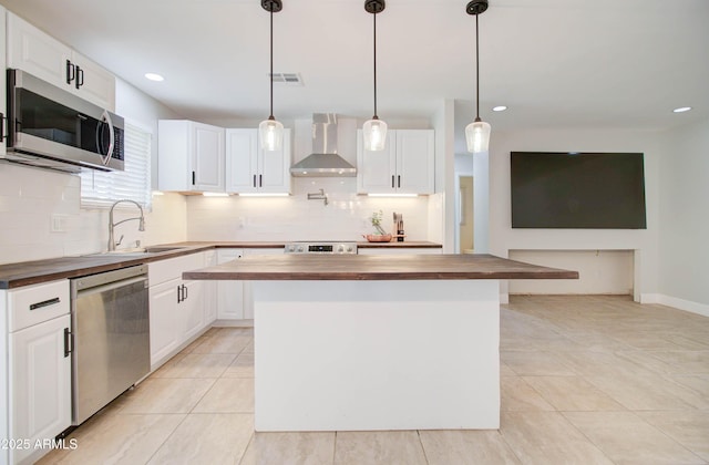 kitchen featuring wall chimney range hood, sink, appliances with stainless steel finishes, white cabinets, and butcher block counters