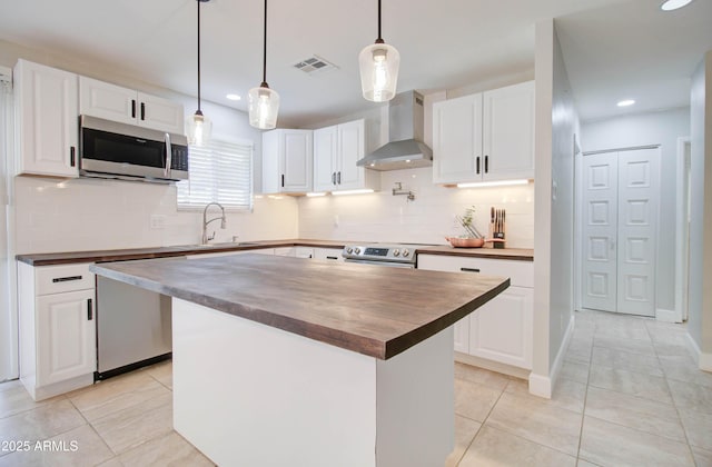 kitchen with white cabinets, a center island, wall chimney exhaust hood, and stainless steel appliances