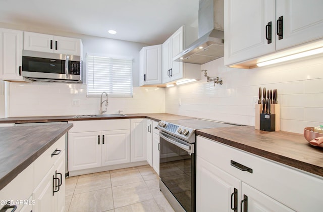 kitchen featuring white cabinetry, wall chimney range hood, butcher block counters, and stainless steel appliances