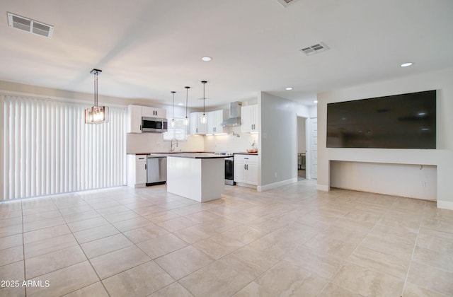 kitchen featuring appliances with stainless steel finishes, white cabinetry, wall chimney exhaust hood, and hanging light fixtures