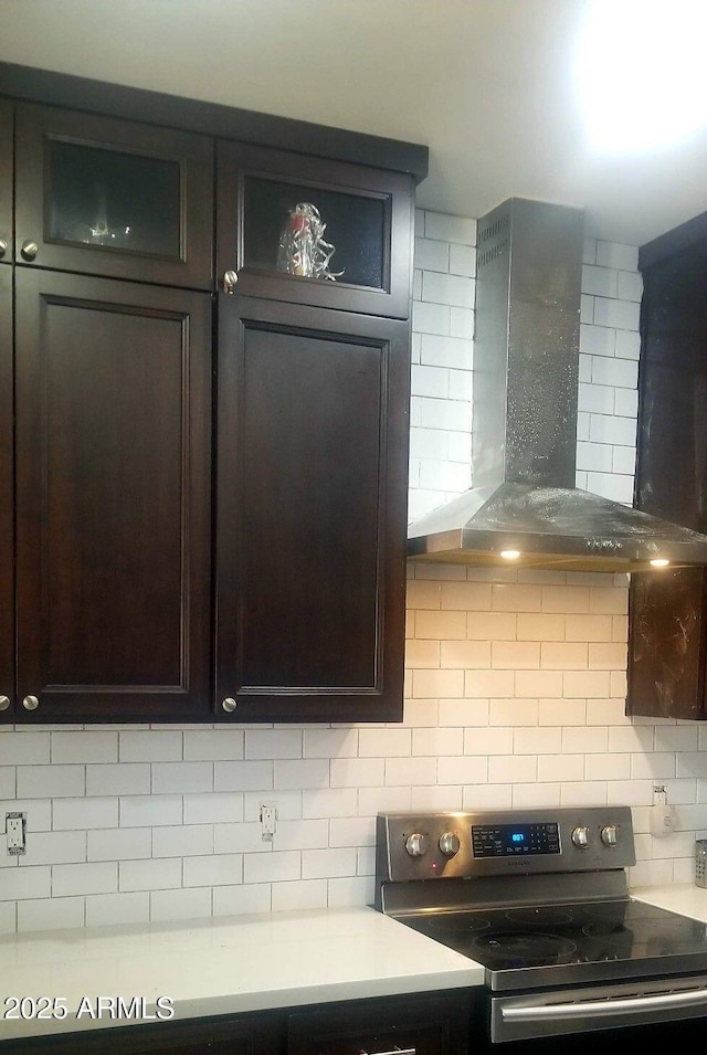 kitchen featuring wall chimney range hood, decorative backsplash, dark brown cabinetry, and stainless steel electric range